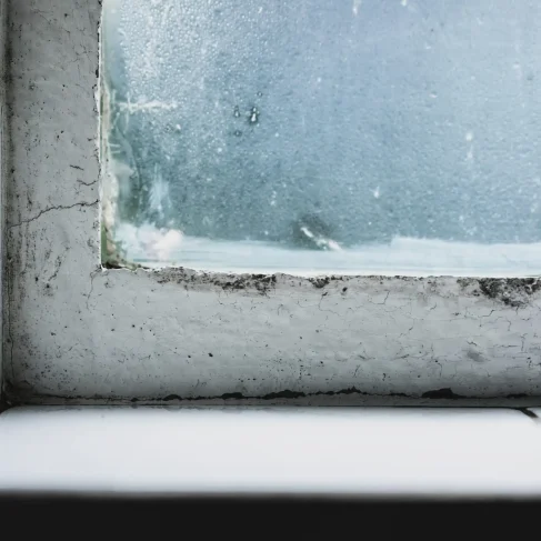 A closeup shot of a wild windowsill with an old window and the glass covered in frosting