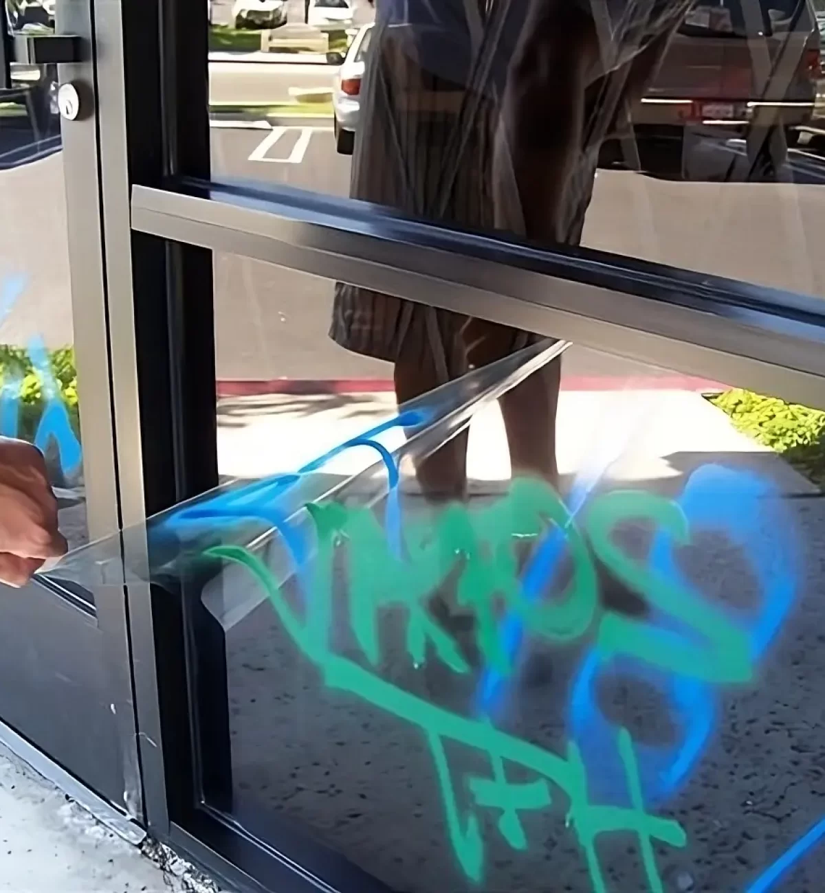 Professionnel en pose de film adhésif retirant un film anti-graffiti couvert de tags sur une vitre