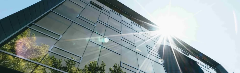 fenêtre de bâtiment baignée de lumière directe du soleil, créant un éblouissement intense à l'intérieur de la pièce. Sans film anti-reflet, la luminosité excessive rend difficile la visibilité à travers la vitre et crée une atmosphère éblouissante et inconfortable. L'absence de protection contre les reflets solaires peut entraîner des niveaux élevés d'éblouissement et une augmentation de la chaleur à l'intérieur.
